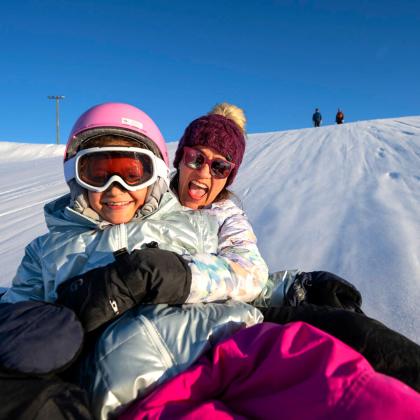 Mom and Daughter are tubing down a steep, snowy slope